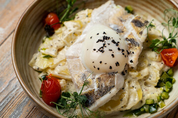 A portion of fish and potato gratin with rich creamy sauce with a poached egg, close very appetizing view