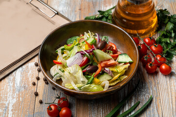 Simple vegetarian salad with olives, lettuce, bell pepper and tomatoes, wooden table with vegetables around