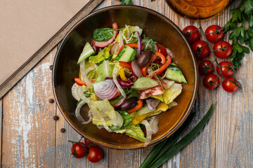 Simple vegetarian salad with olives, lettuce, bell pepper and tomatoes, wooden table with vegetables around
