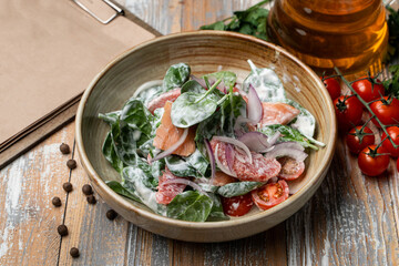 Summer salad with spinach, tomatoes, cucumbers and bell pepper with mayonnaise, served in a rustic clay table