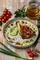 Stuffed aubergine, totally vegan meal in a restaurant, served on wooden table with vegetables and spices laying around