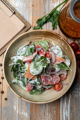 Vegetable salad with spinach, tomatoes, cucumbers and bell pepper with mayonnaise, wooden background with spices around