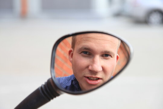 Portrait of a man in a mirror image.A comical, cheerful, cheerful guy in the mirror from a motorcycle. High quality photo