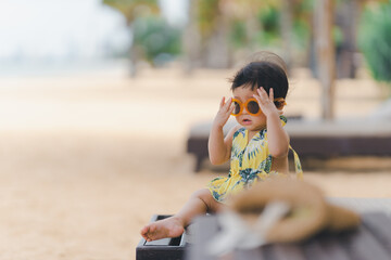 Little baby with orange sunglasses sitting on a beach chair