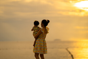 Mother holding baby standing with lonely Emotional at sea in the evening with beautiful sunset