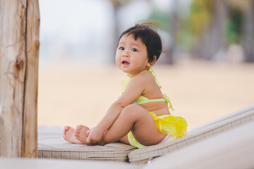 A cute little girl in a yellow two-piece bathing suit sits in a relaxed pose on the beach.