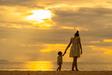 Mother and baby take a walk on the beach with a beautiful sunset.