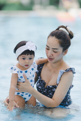 Mother and baby are very happy playing together in the swimming pool on vacation.
