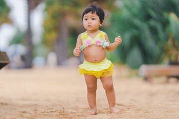 Adorable little girl in a yellow two-piece swimsuit stands in a relaxed pose at the beach.