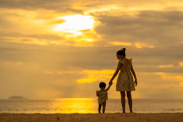 Mother and baby take a walk on the beach with a beautiful sunset.