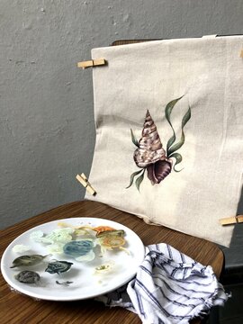 Tote bag with a sea shell painted on it drying on a chair