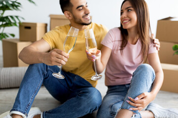 Young interracial couple having housewarming party, celebrating new home purchase, drinking champagne on moving day