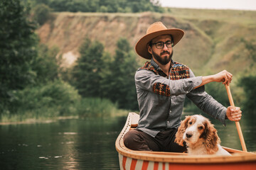 Young man in hat on the river in wooden canoe with his dog