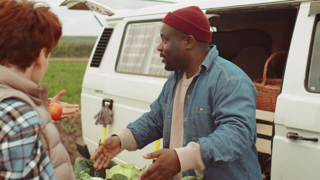 Two young Caucasian women buying fresh vegetables and speaking with African American farmer at van market