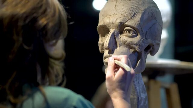 Woman sculptor at work on a sculpture of a human head. The process of restoring the shape of the lips. Side view. Close up view.