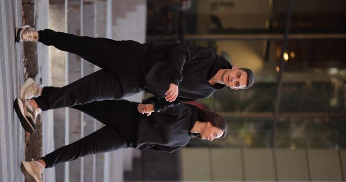 Fashionable couple in black costumes cross the road in a city, vertical video, slow motion