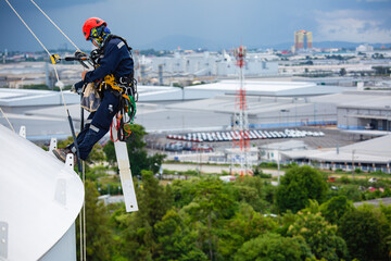 Male workers control rope down top roof tank rope access inspection of thickness shell plate...