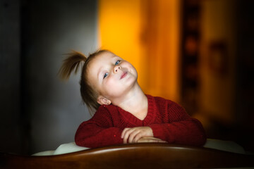 Cute funny caucasian child girl in a red dress on an armchair, dark style, christmas and new year concept