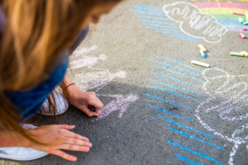teenage girl drawing a rainbow colored chalk on the asphalt on summer day