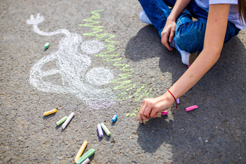 Little girl with creative craft hobby drawing electro on the asphalt with chalk car environment, eco friendly, save energy in park at summer day