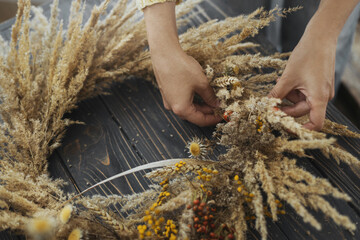 Making stylish autumn wreath. Hands holding dry grass, wildflowers and wheat and making rustic...