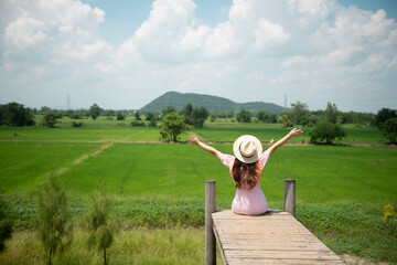 woman sitting on the wooden brigde and look at the Rice Field. Summer Country Vacation and Adventure Concept.
