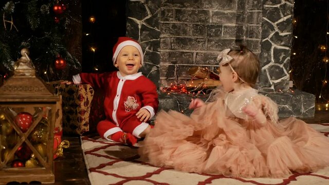 One-year-old brother and sister play at home near the Christmas tree and celebrate Christmas.
