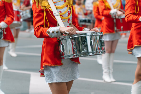 Street Performance Of Festive March Of Drummers Girls In Red Costumes On City Street. Young Girls Drummer In Red Vintage Uniform At The Parade