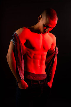 Neon light red studio close-up portrait of attractive male model portrait photo of a dark-skinned handsome guy. The muscular egyptian male on black background. Sexy naked torso. 