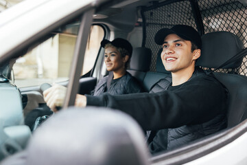 Two delivery coworkers sitting in van. Smiling courier driving a car.