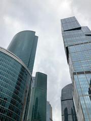 Fototapeta premium Facade of modern skyscraper with glass walls. From below of contemporary tall skyscraper with glass walls against cloudy sky in downtown