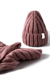 Small red knitted hat with on a white scarf on white isolated background. woolly hat Closeup.