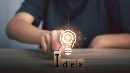 Innovation idea and knowledge concept. Hand touch gear icon in light bulb icon of ​​inspiration thinking with text  i d e a in woods block.