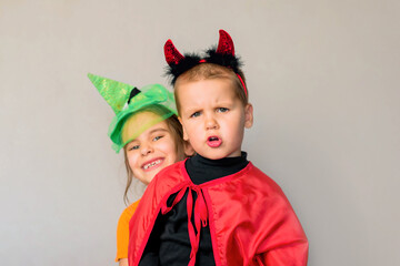 One little toddler boy and girl in a carnival costume for Halloween is isolated on a grey background. Traditions, holidays concept.