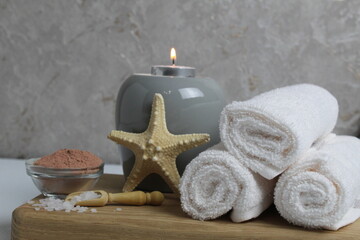 Obraz na płótnie Canvas Spa relax massage home body care. White towels oil fragrant for massage aromatherapy candles star sea lie on a wooden tray on a gray background side view