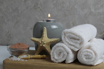 Fototapeta na wymiar Spa relax massage home body care. White towels oil fragrant for massage aromatherapy candles star sea lie on a wooden tray on a gray background side view