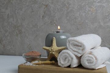 Fototapeta na wymiar Spa relax massage home body care. White towels oil fragrant for massage aromatherapy candles star sea lie on a wooden tray on a gray background side view