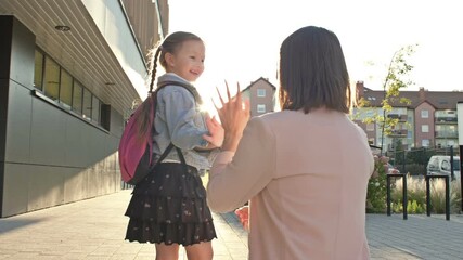 Young woman accompanies her little daughter to school. The schoolgirl kisses her mother goodbye and happily runs to class.