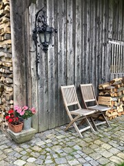 Zwei Gartenstühle an einem Holzschuppen und aufgeschlichtetes Brennholz 