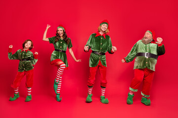 Full length photo of happy, elf people dance celebrate xmas wear hat costume enjoy isolated on red color background - obrazy, fototapety, plakaty