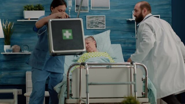 Doctor and nurse rushing to help sick patient with resuscitation in nursing home. Senior woman with disease in bed receiving medical support from specialists with medical equipment.