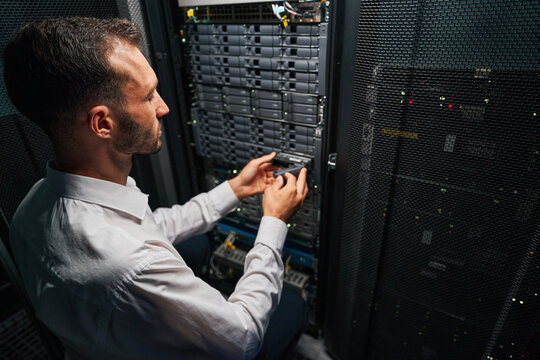 Handsome Caucasian system administrator controlling operational server rack in room indoors