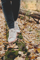 crop view of woman legs walking along the tree trunk. autumn in the forest, local travel, spending time in a park. casual clothes and sneakers.