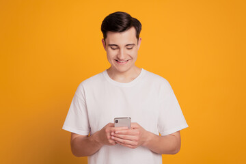 Portrait of positive handsome guy hold phone look screen typing message white smile on yellow background