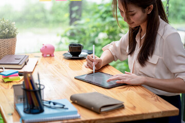 Young Asian businesswoman holding a stylus working on a tablet at the office.