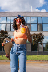 happy african american woman in headscarf holding plastic cup with orange juice and longboard outside © LIGHTFIELD STUDIOS