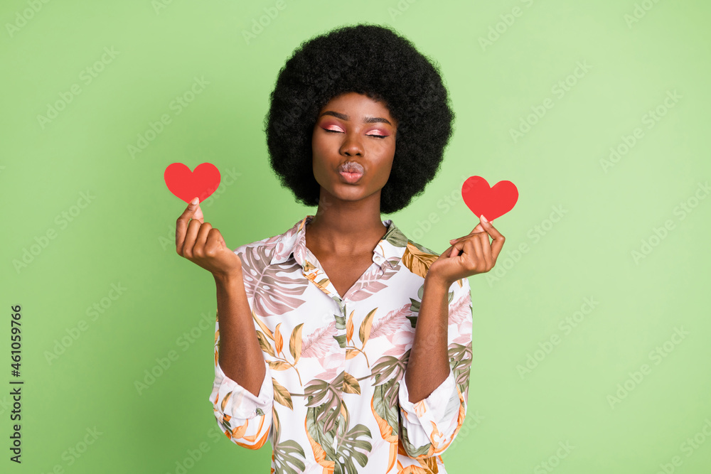 Sticker Photo of young afro girl pouted lips send air kiss you hold paper heart card gift isolated over green color background