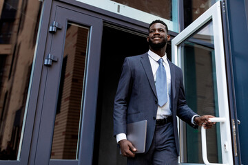 Young african american entrepreneur man leaving business center building after work, looking away, copy space