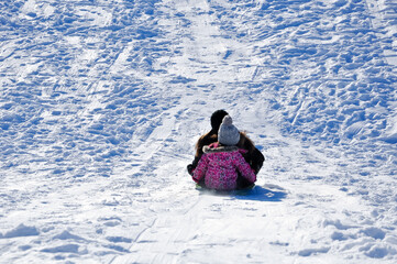 Mother and daughter tobogganing in the snow