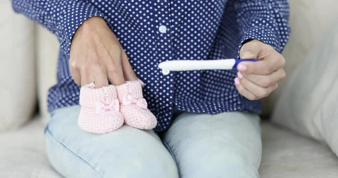 Woman sitting on sofa with pregnancy test and holding pink booties 4k movie
